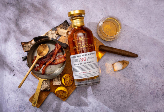 A bottle of Queen of the Hebrides Blended Malt Scotch Whisky sits upon a concrete table top surrounded by tasting notes.