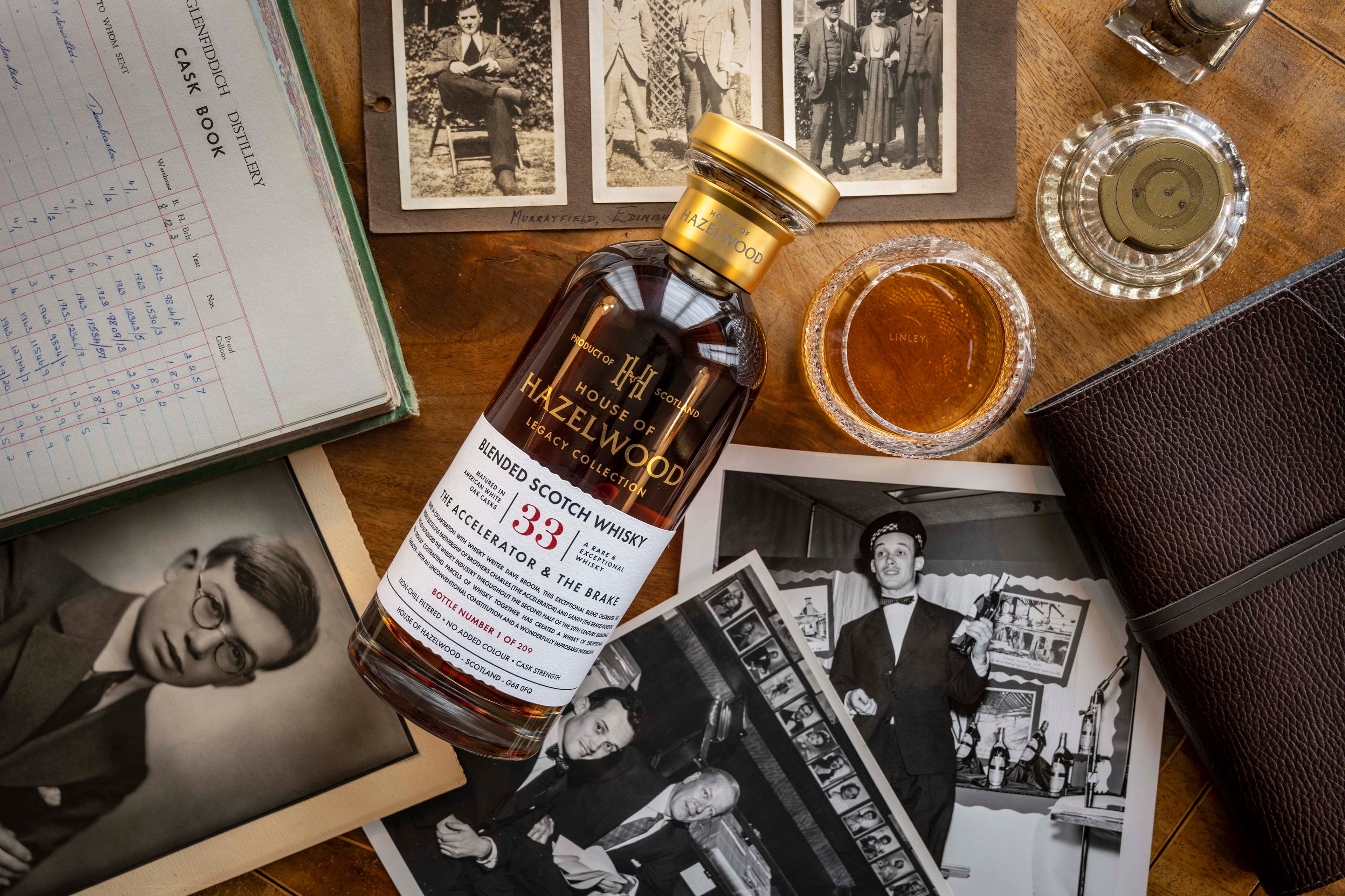 A bottle of The Accelerator & The Brake Whisky lying on a desk with a pour of the whisky and images of brothers Charles & Sandy Gordon who inspired the blend.